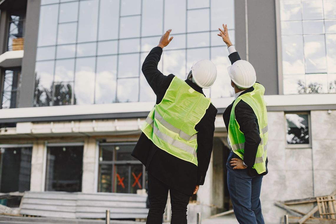 Two construction workers are standing in front of a building under construction.