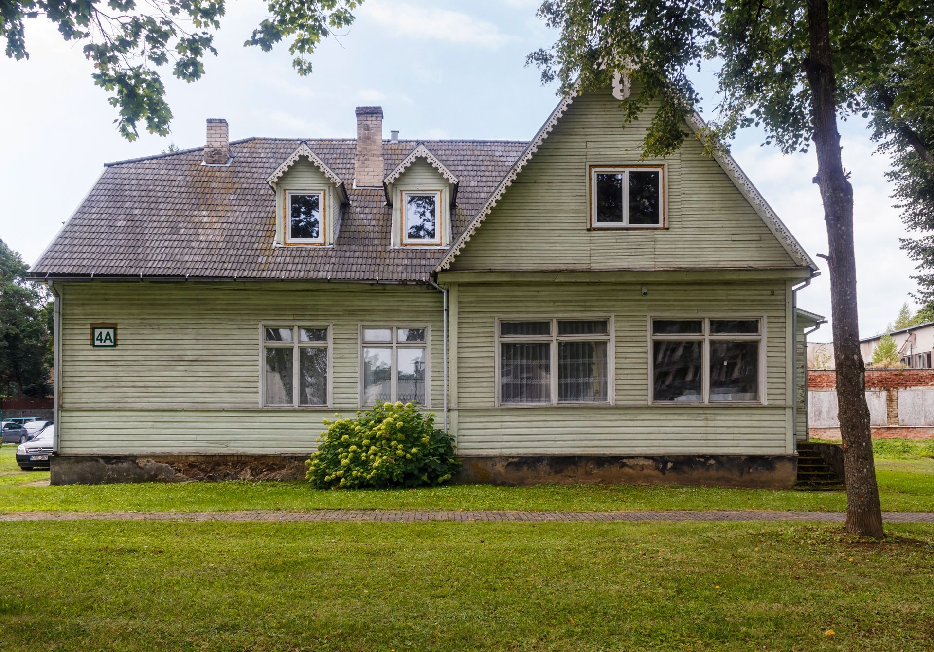 A large white house with a gray roof is sitting in the middle of a lush green field.