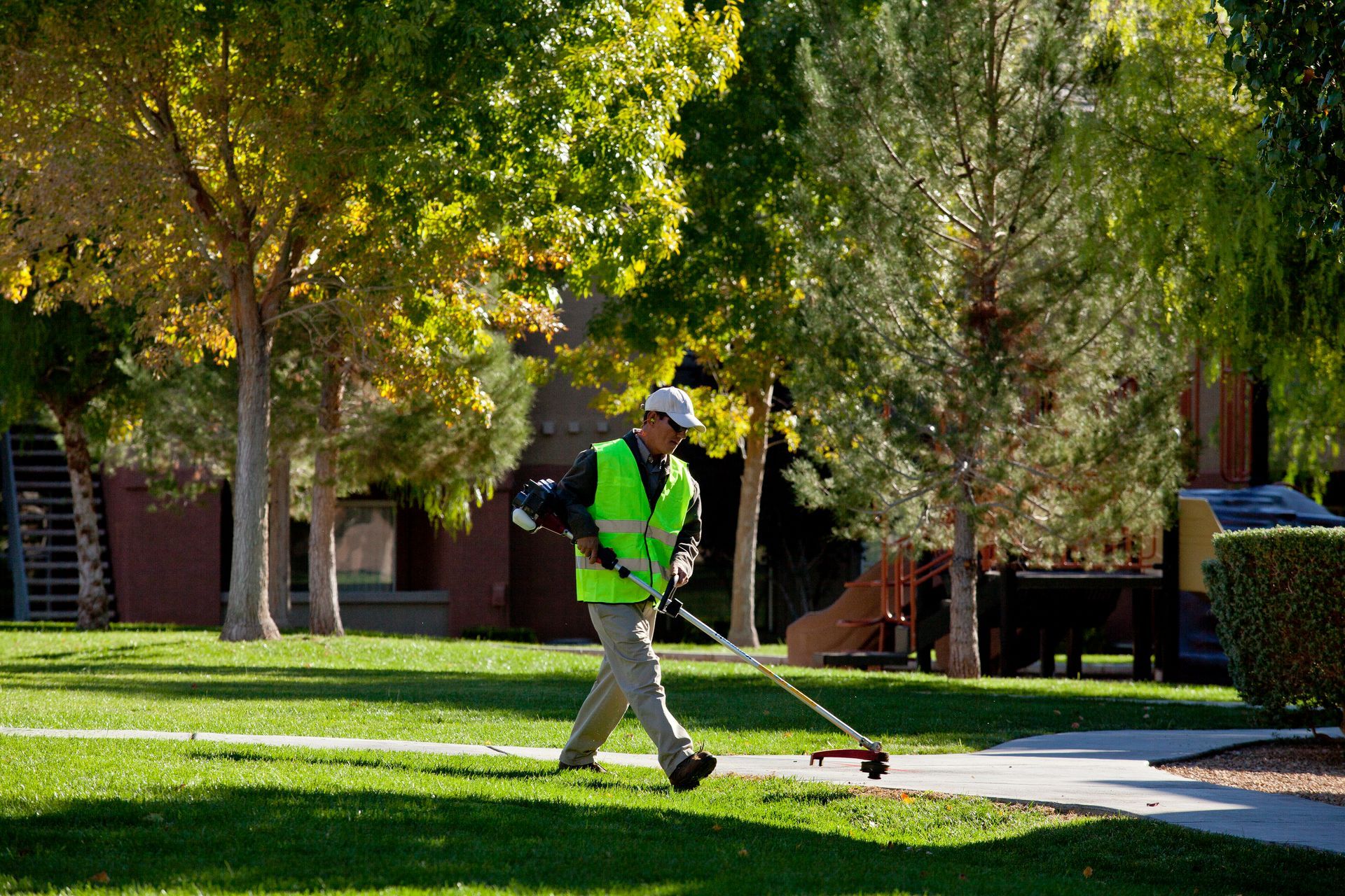 A man is using a lawn mower to cut the grass in a park.
