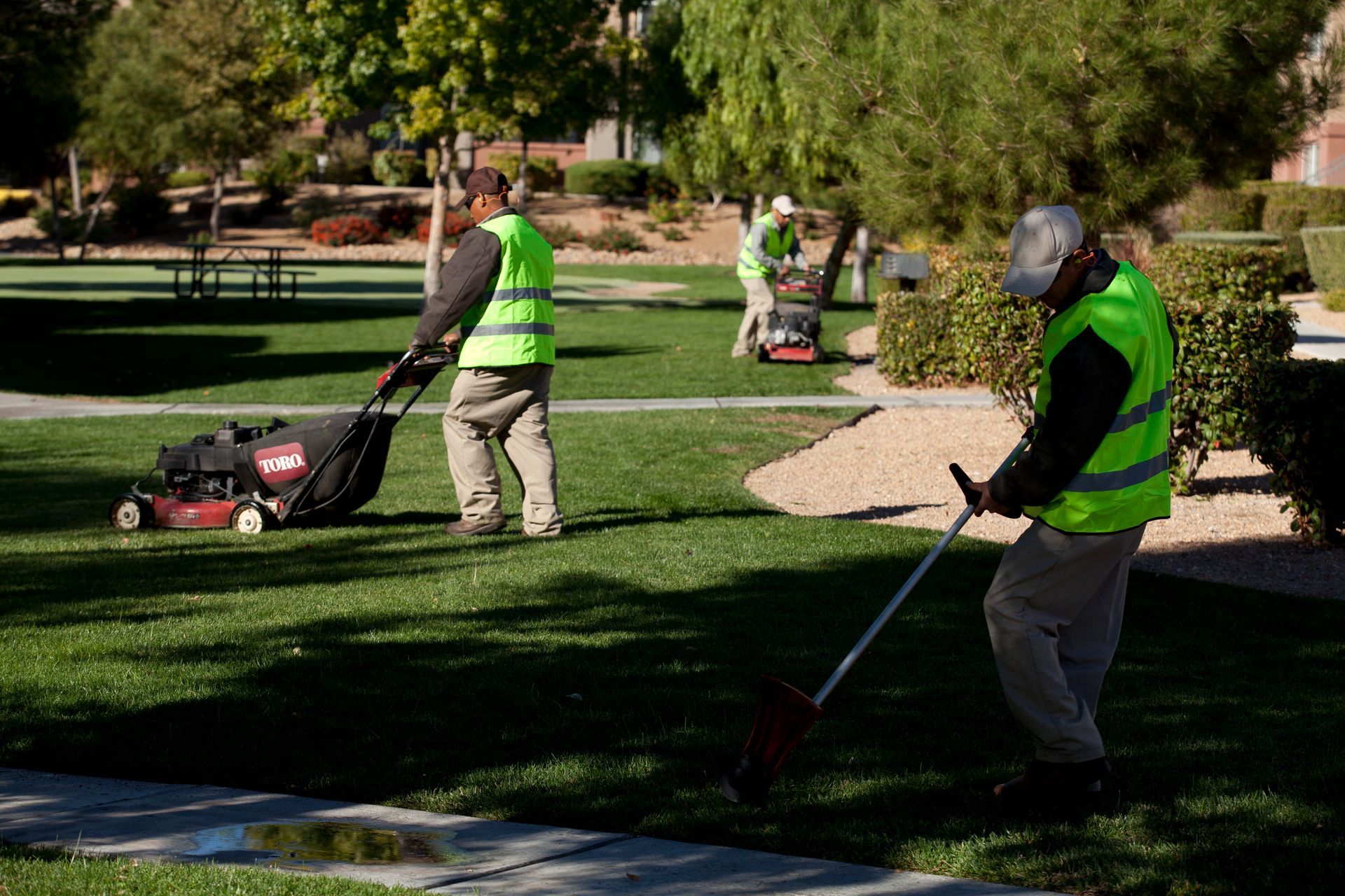 Two men are mowing the grass in a park.