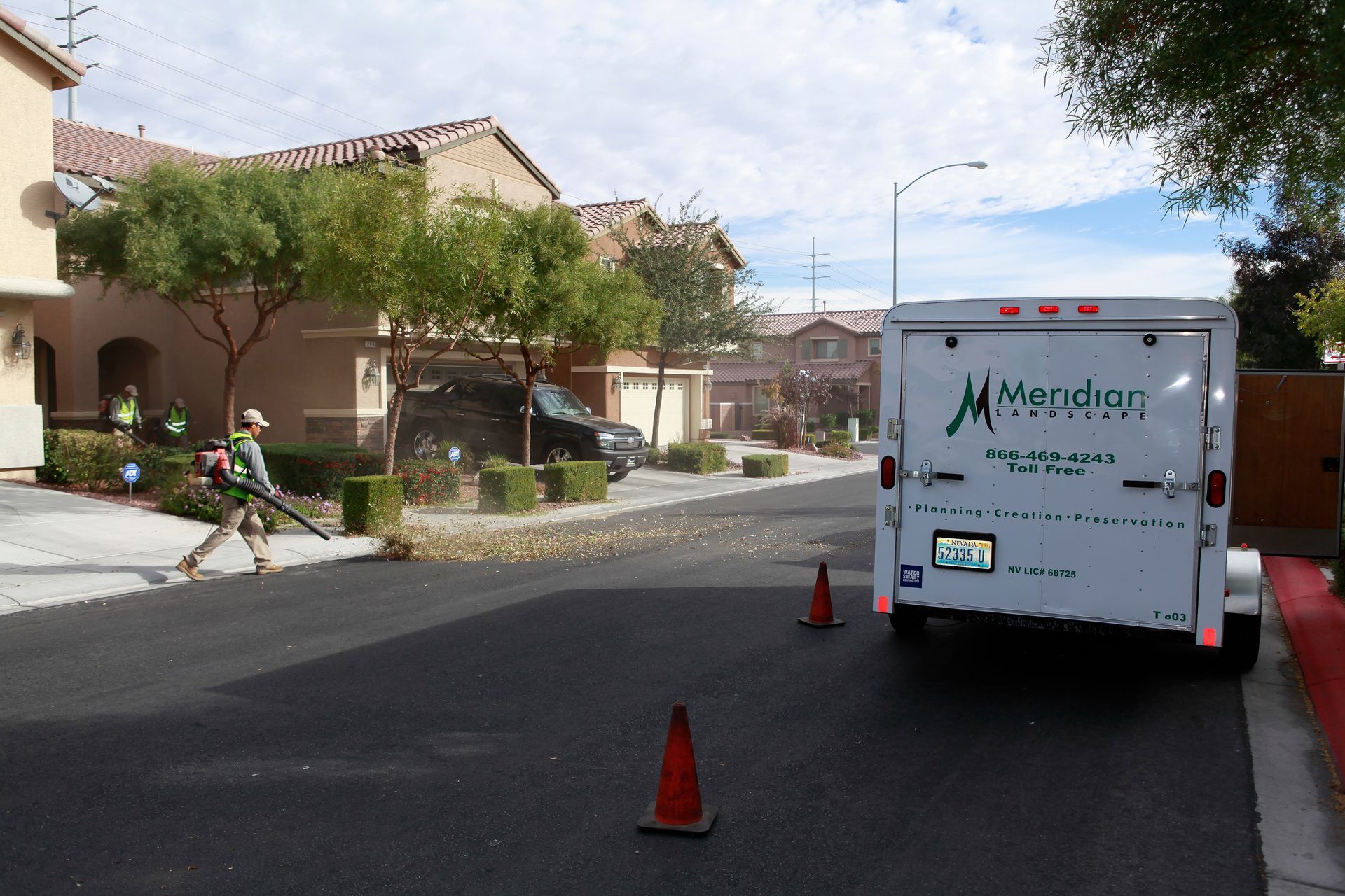 A man is using a lawn mower on the side of the road next to a trailer that says morgan