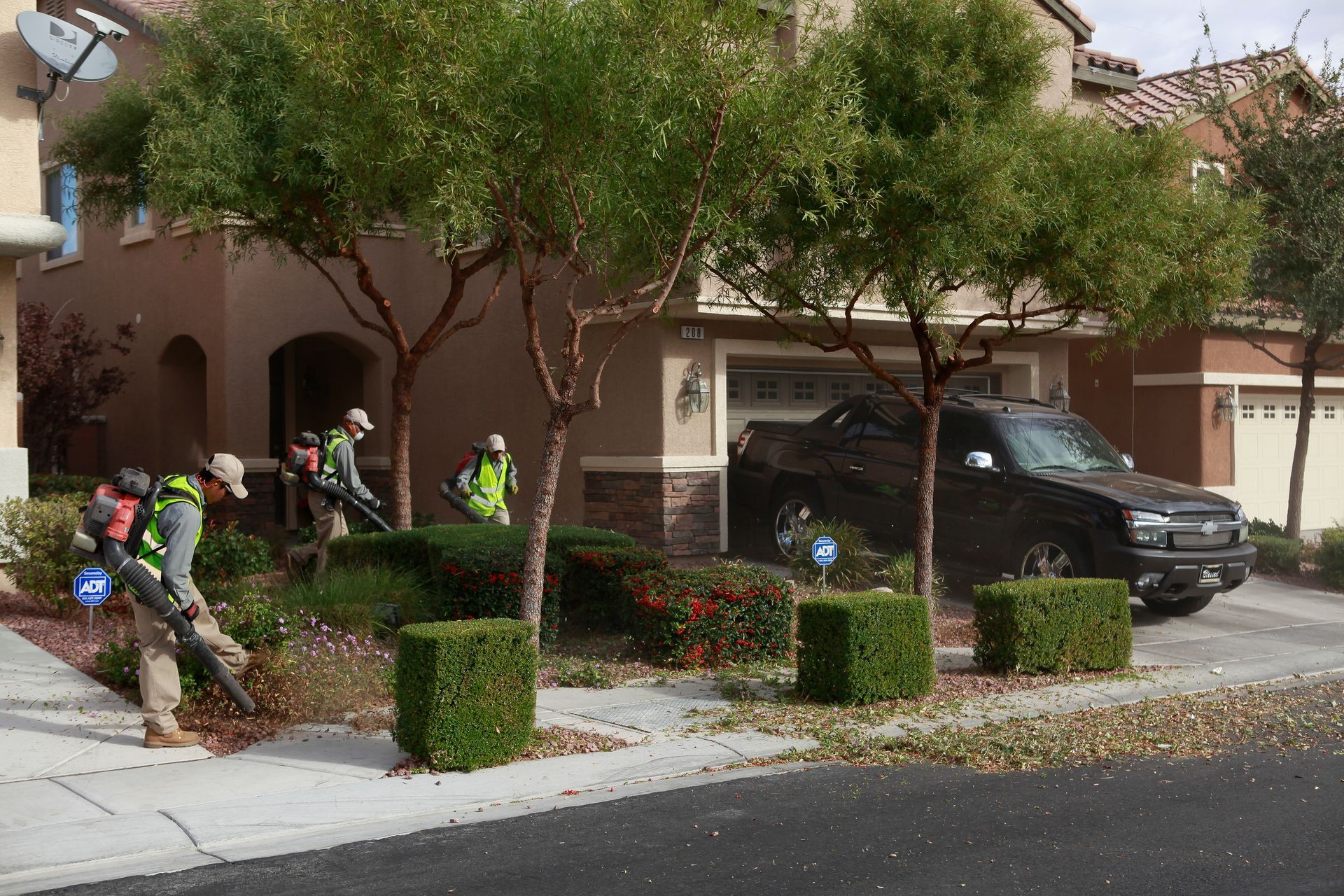 A man is blowing leaves on the sidewalk in front of a house.