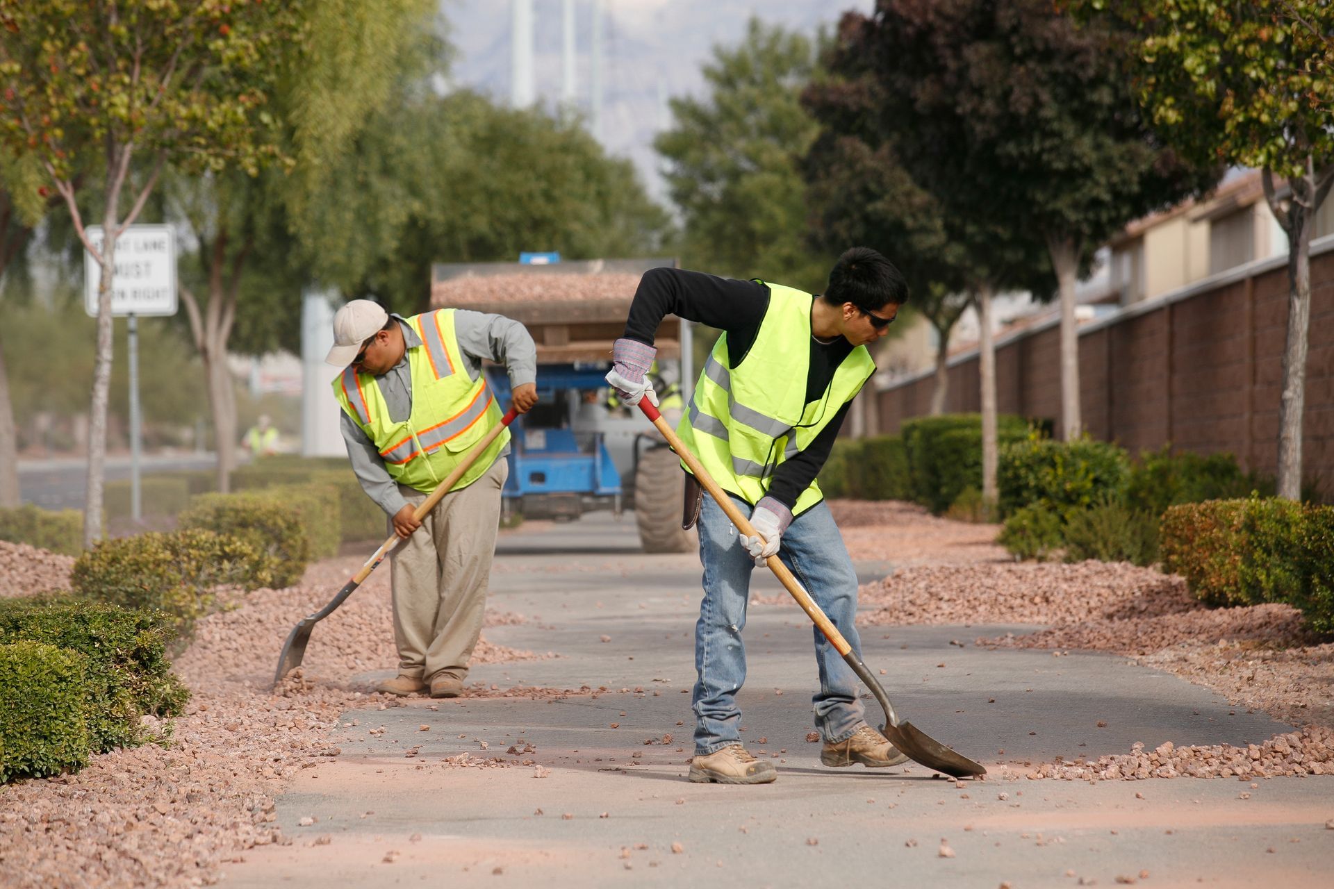 Two men are cleaning the sidewalk with rakes and shovels.