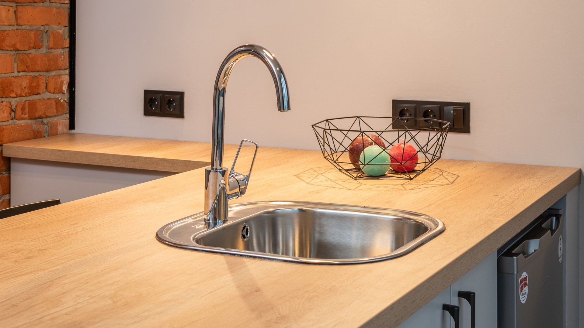 A kitchen sink with a faucet and a basket of fruit on the counter.