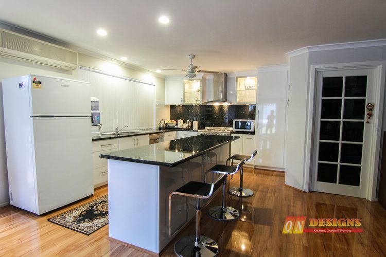 A kitchen with a large island and stools and a refrigerator.