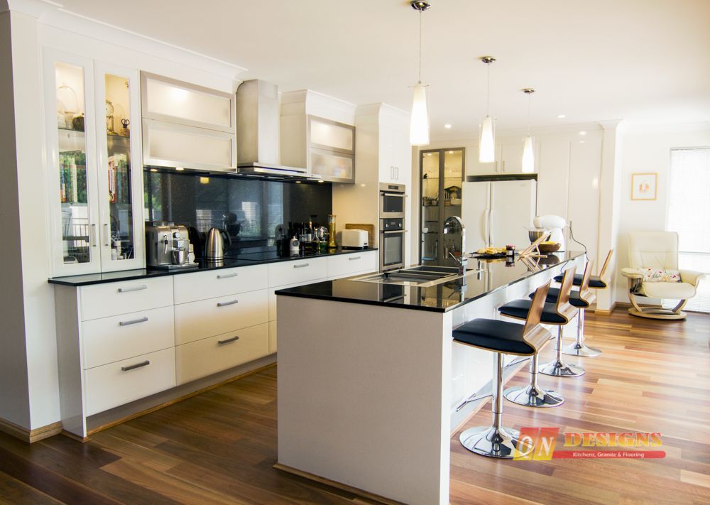 A kitchen with white cabinets and black counter tops and stools.