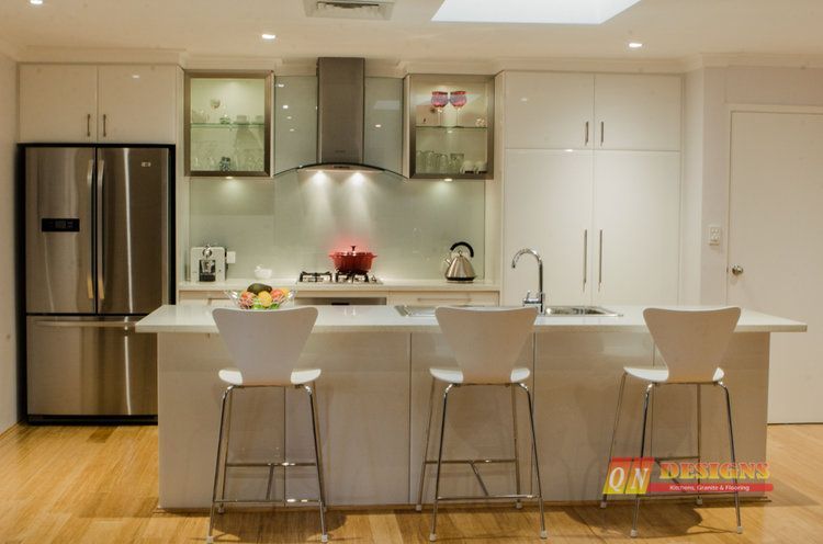 A kitchen with white cabinets and stools and a stainless steel refrigerator