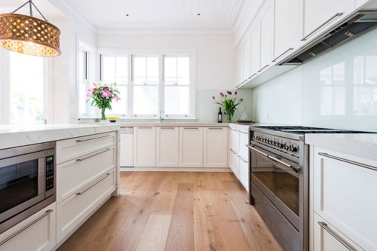 A kitchen with white cabinets , stainless steel appliances , wooden floors and a stove.