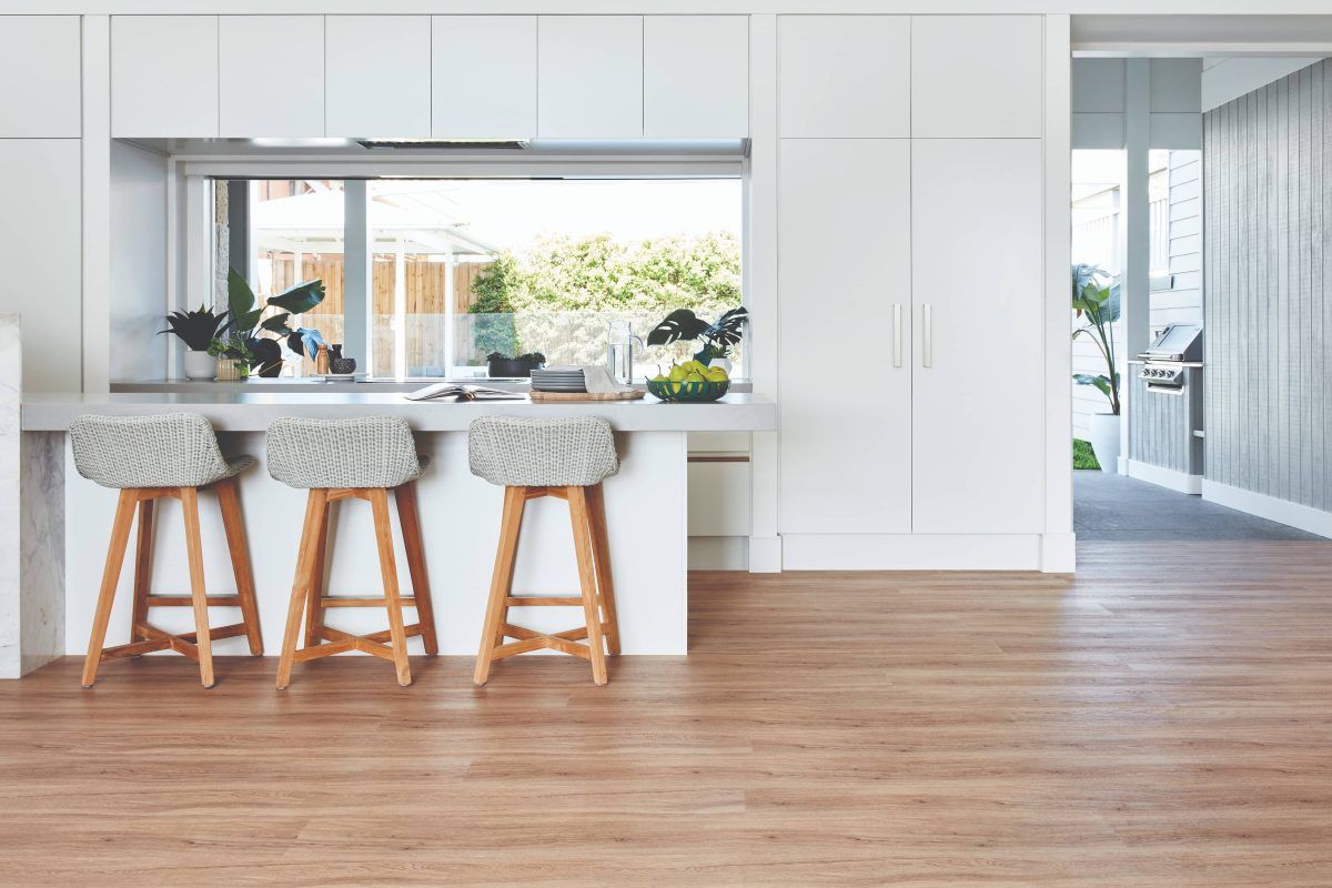 A kitchen with white cabinets and wooden floors and three stools.