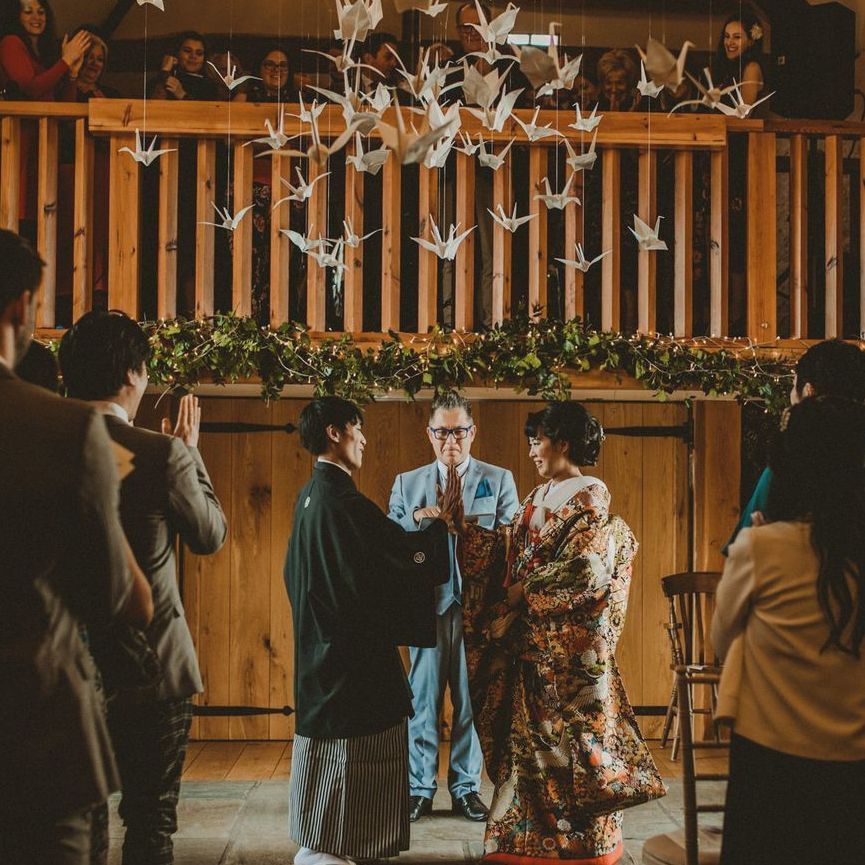 A couple standing at the front of the barn under origami birds doing their vows