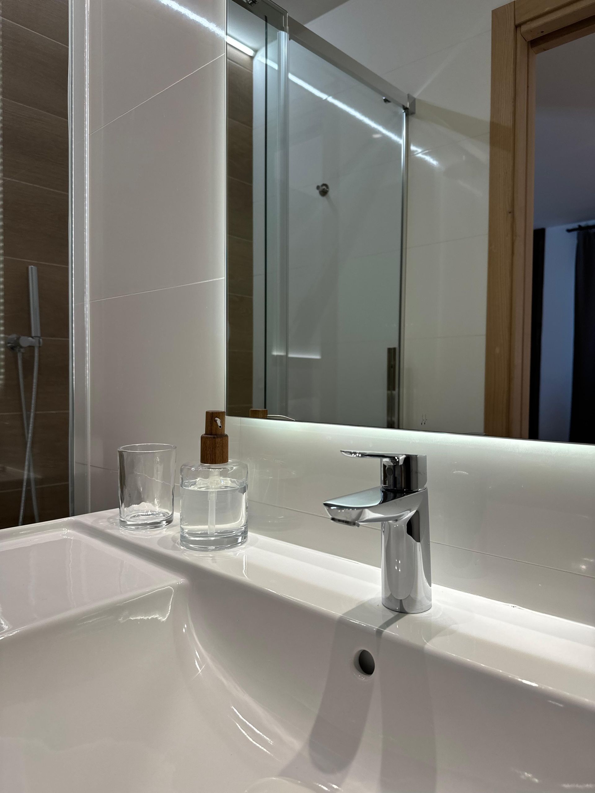 Lavabo con grifo cromado, dispensador de jabón y cristal. Espejo con reflejo de ducha.