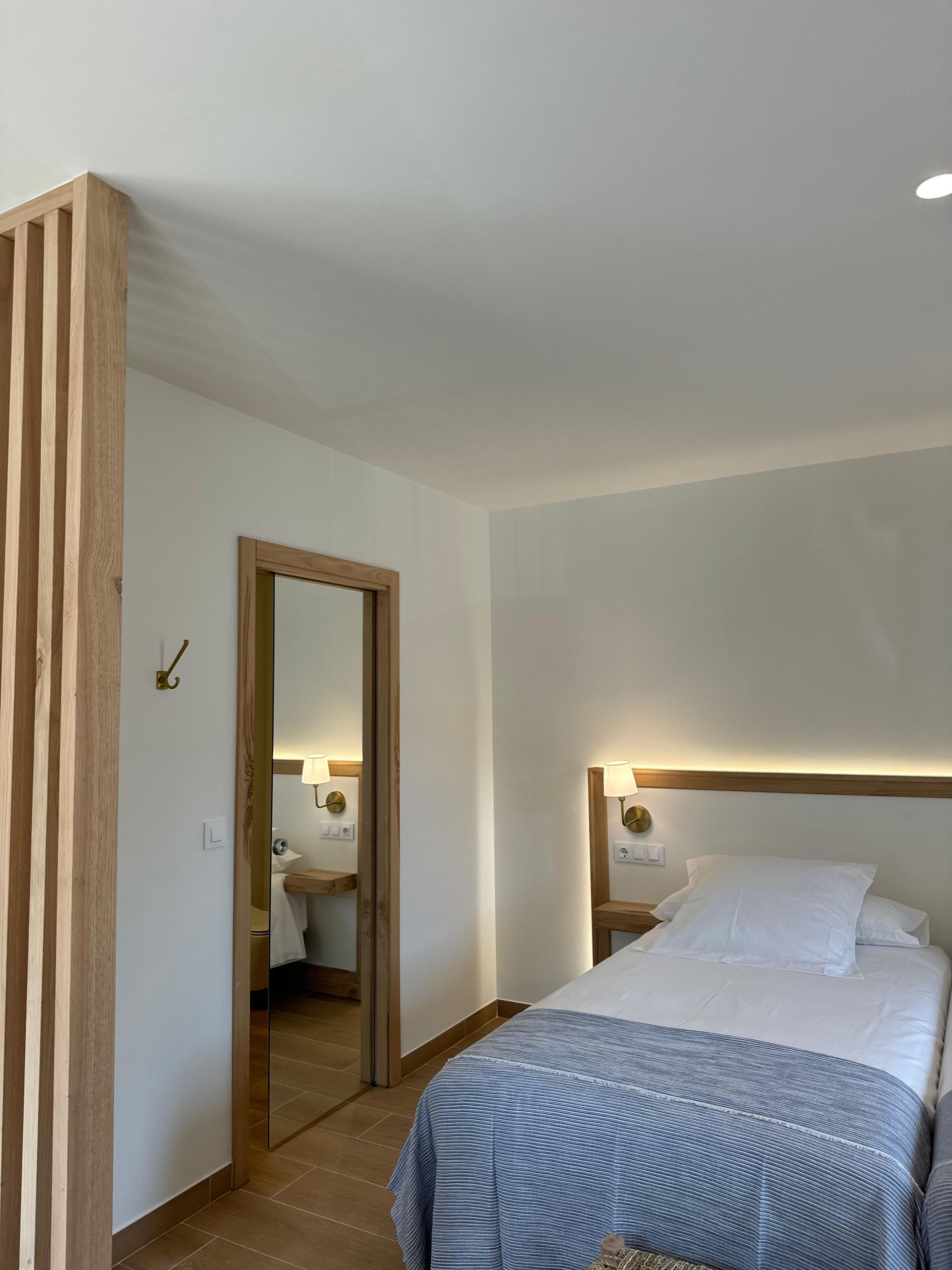 Dormitorio con dos camas, biombo de madera y puerta de acceso a baño con lavabo.