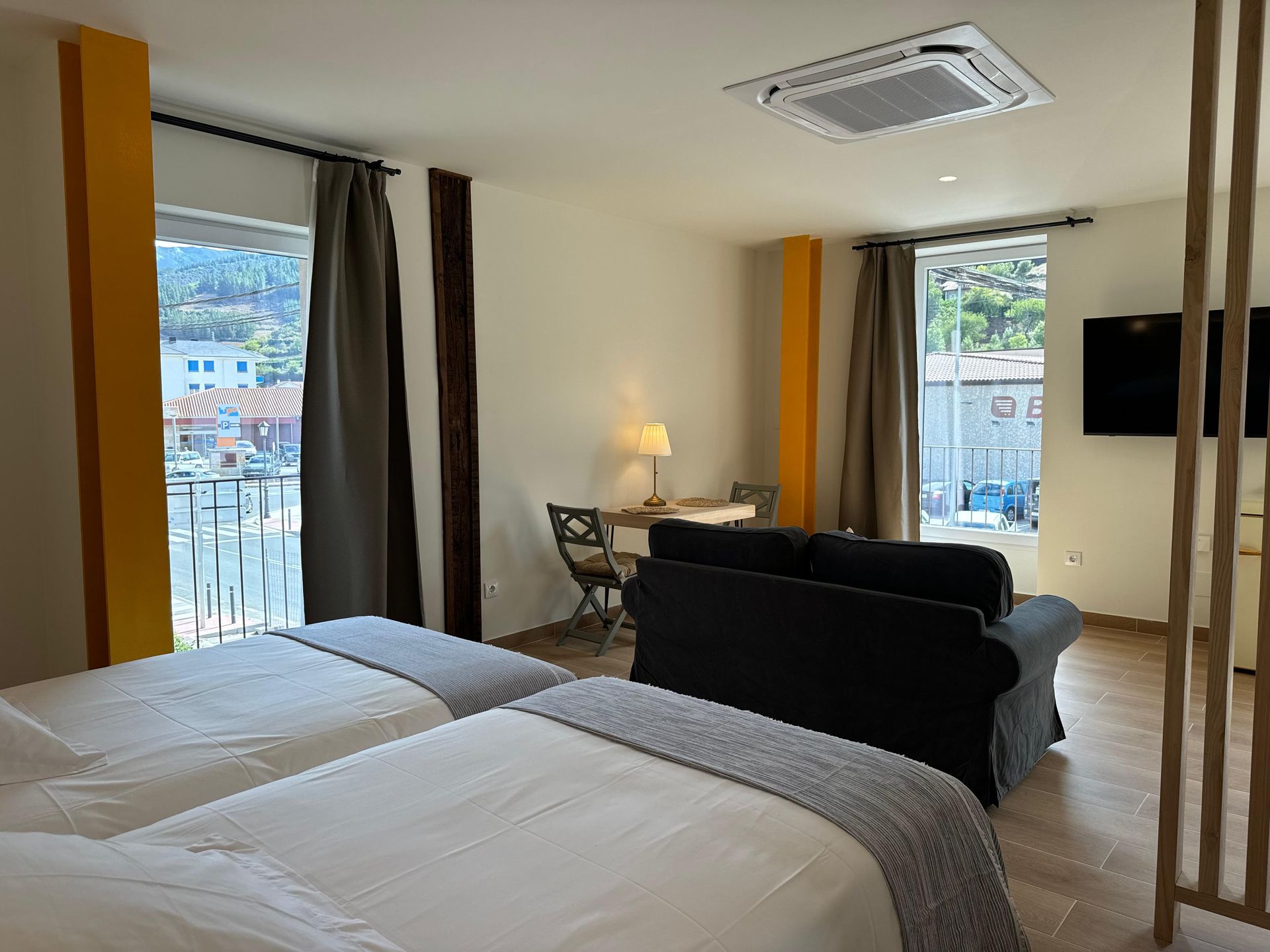 Habitación de hotel luminosa con dos camas, un pequeño sofá y una mesa cerca de ventanas con vistas.
