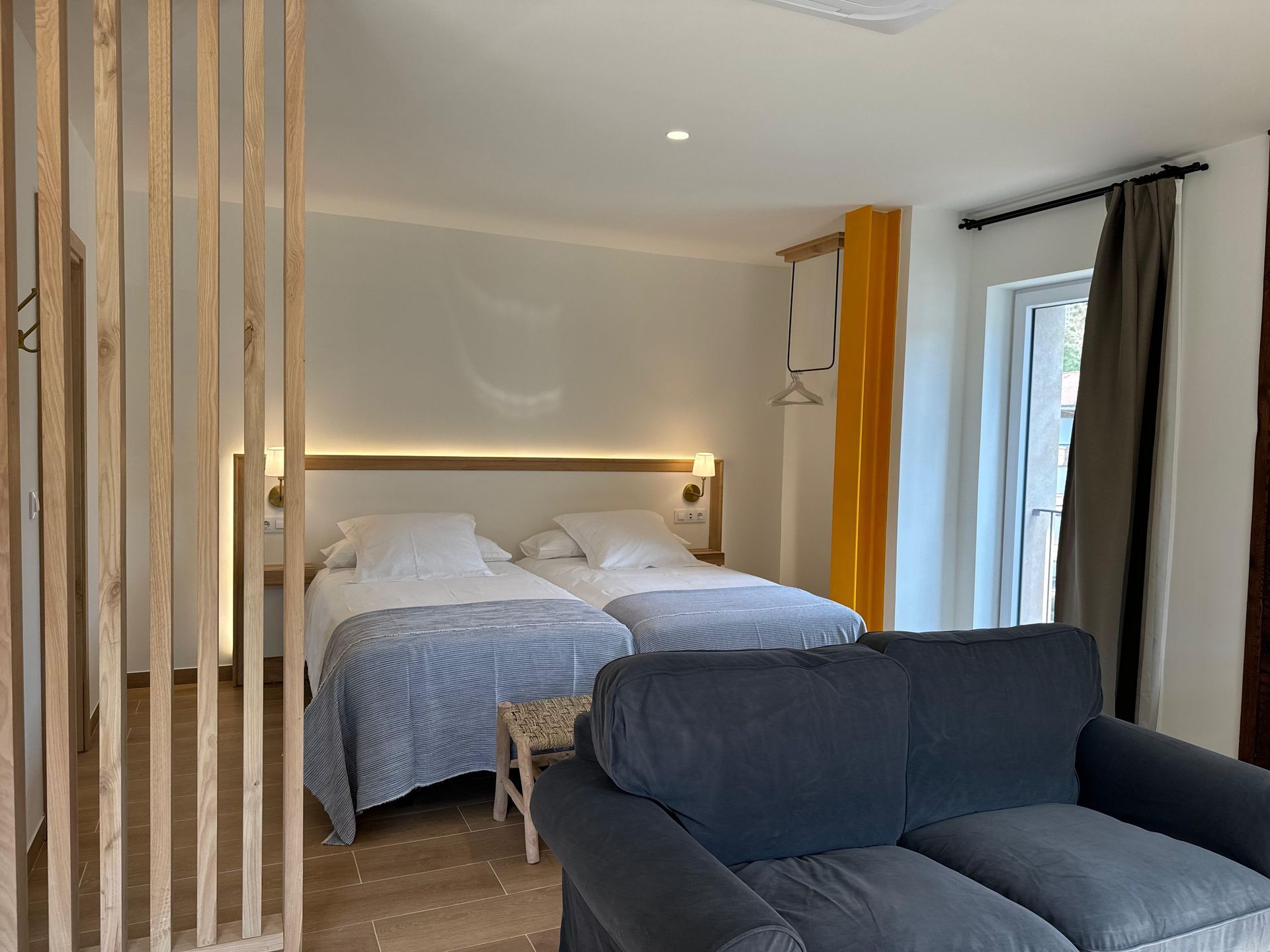 Dormitorio con dos camas individuales, sofá y biombo decorativo de madera. Detalles en blanco y amarillo.