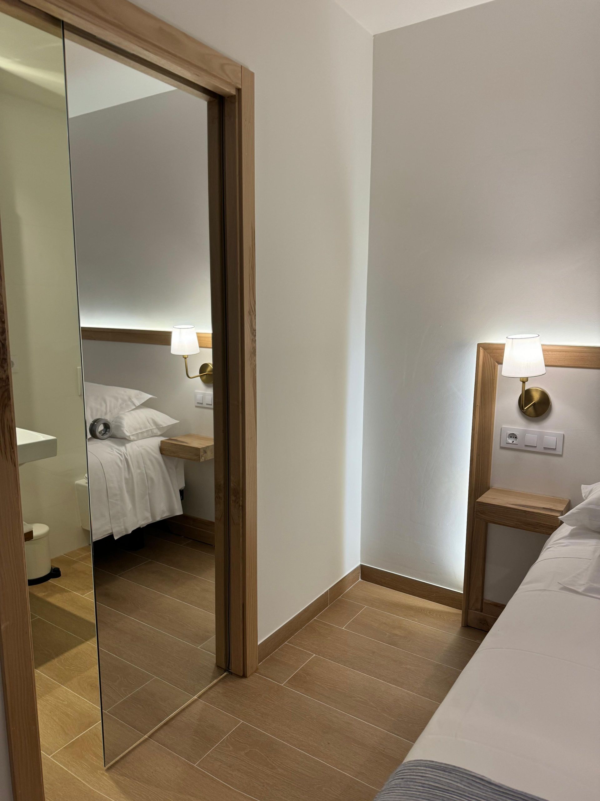 Dormitorio con dos camas, una en primer plano y otra visible a través de una puerta. Iluminación suave y colores neutros.
