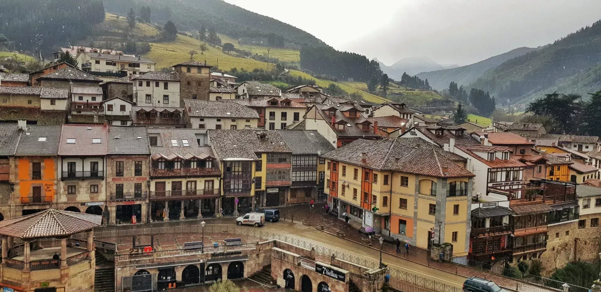 Un pueblo enclavado en un valle con edificios coloridos y un puente, bajo un cielo nublado.