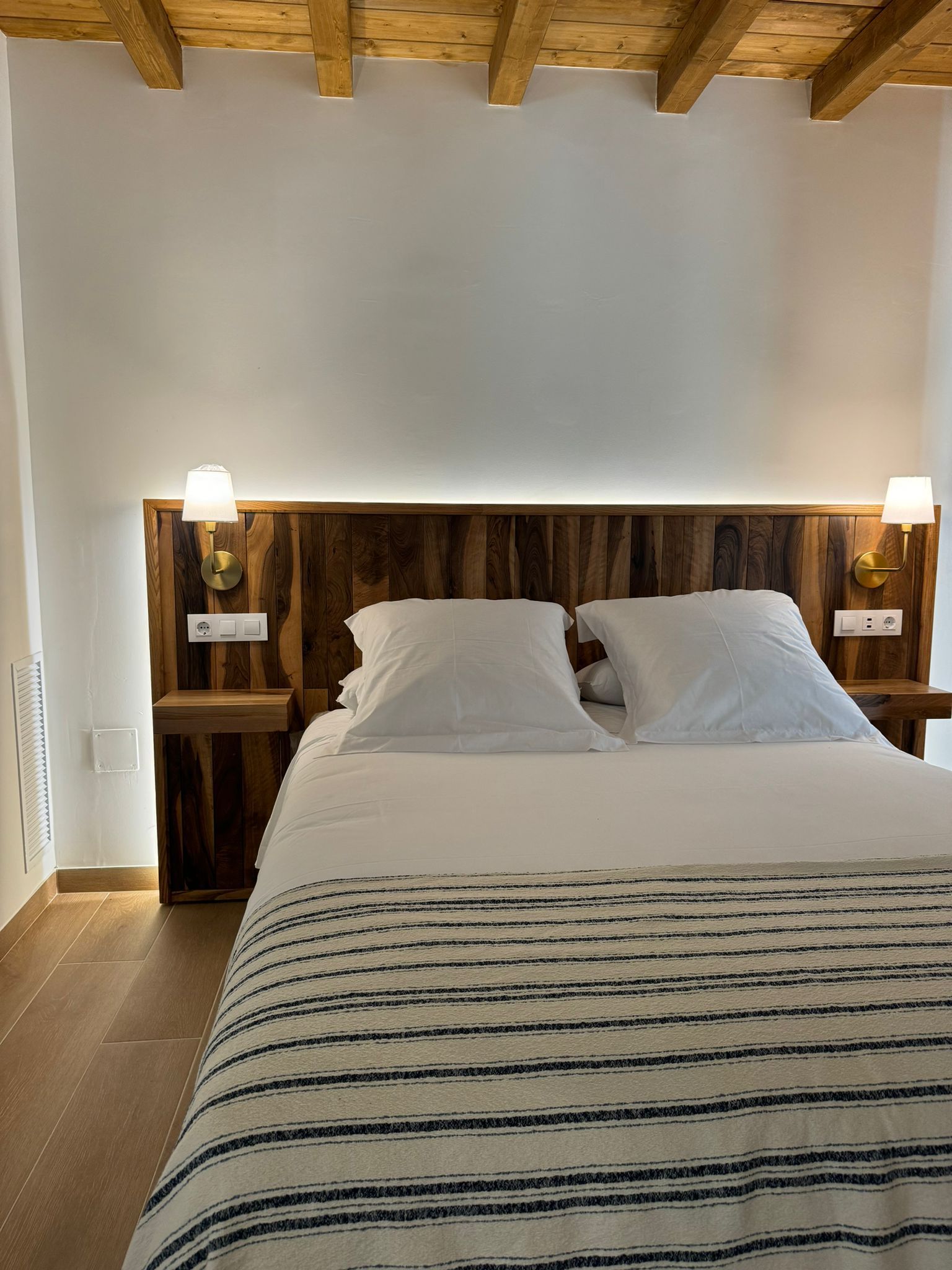 Dormitorio con cabecero de madera, dos almohadas, cama y dos lámparas de mesa.