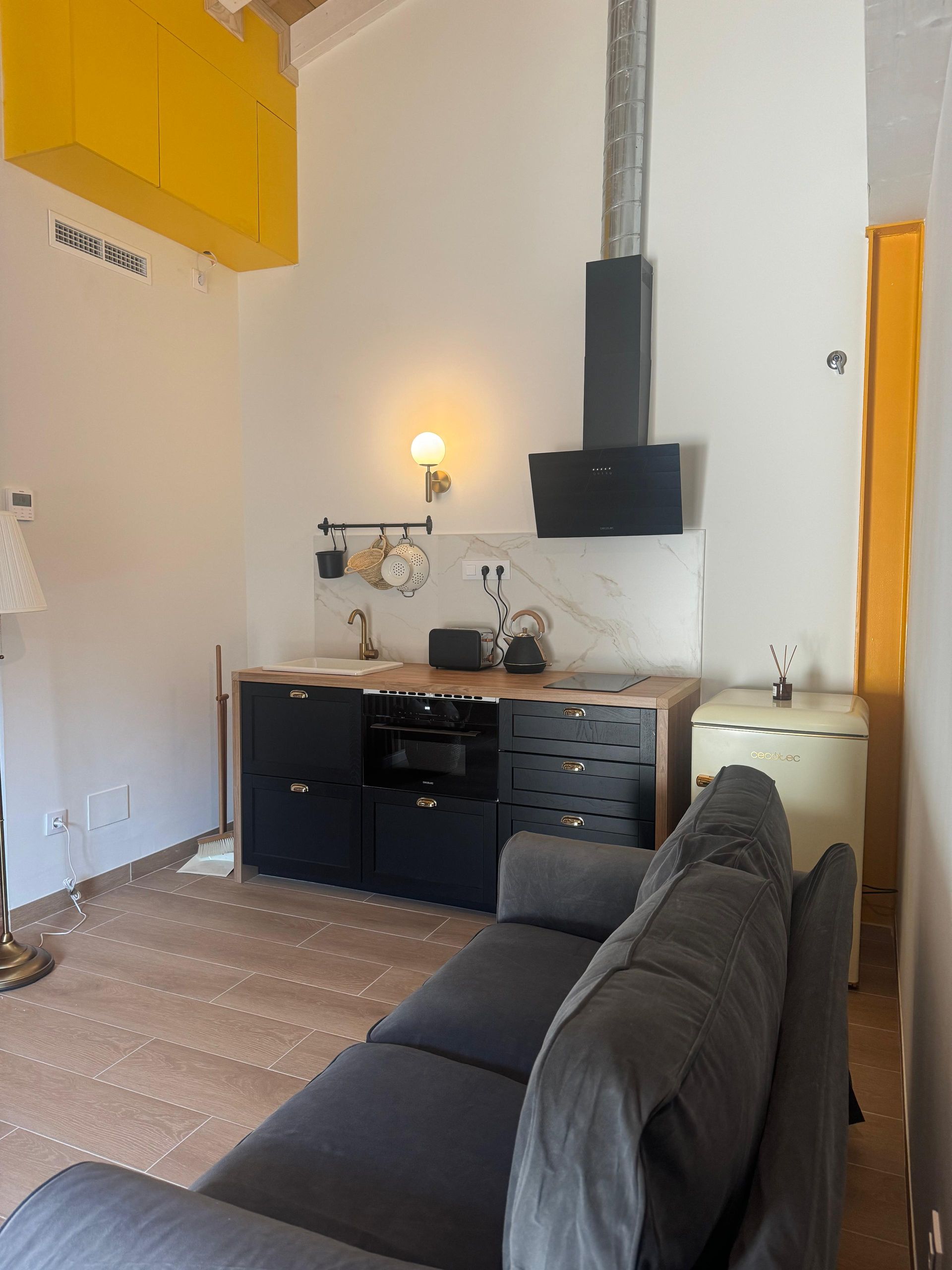 Cocina pequeña con gabinetes negros, sofá y detalles amarillos.