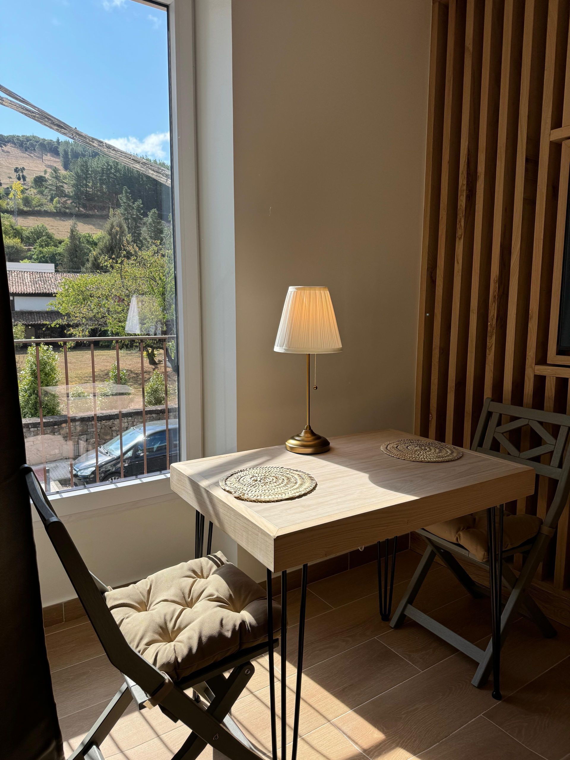 Escritorio con lámpara, dos sillas, cerca de ventana con vista a la montaña.