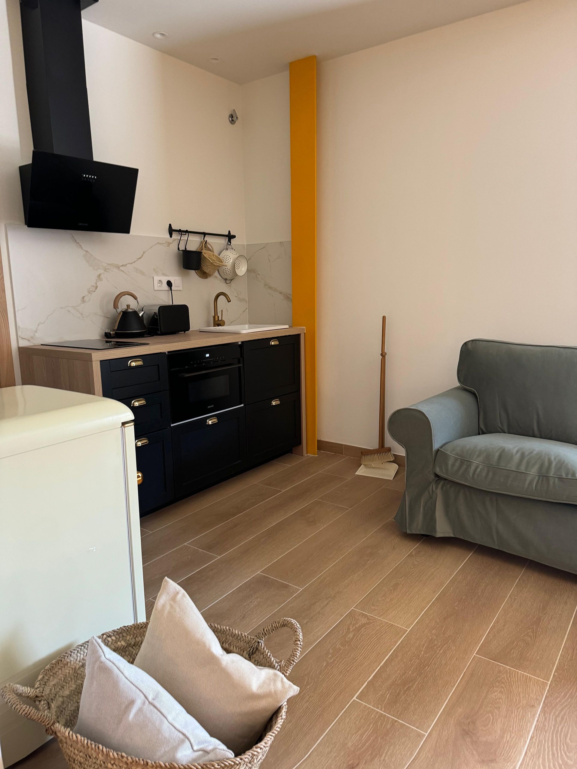Cocina de apartamento pequeño con gabinetes negros, salpicadero de mármol y un sofá.