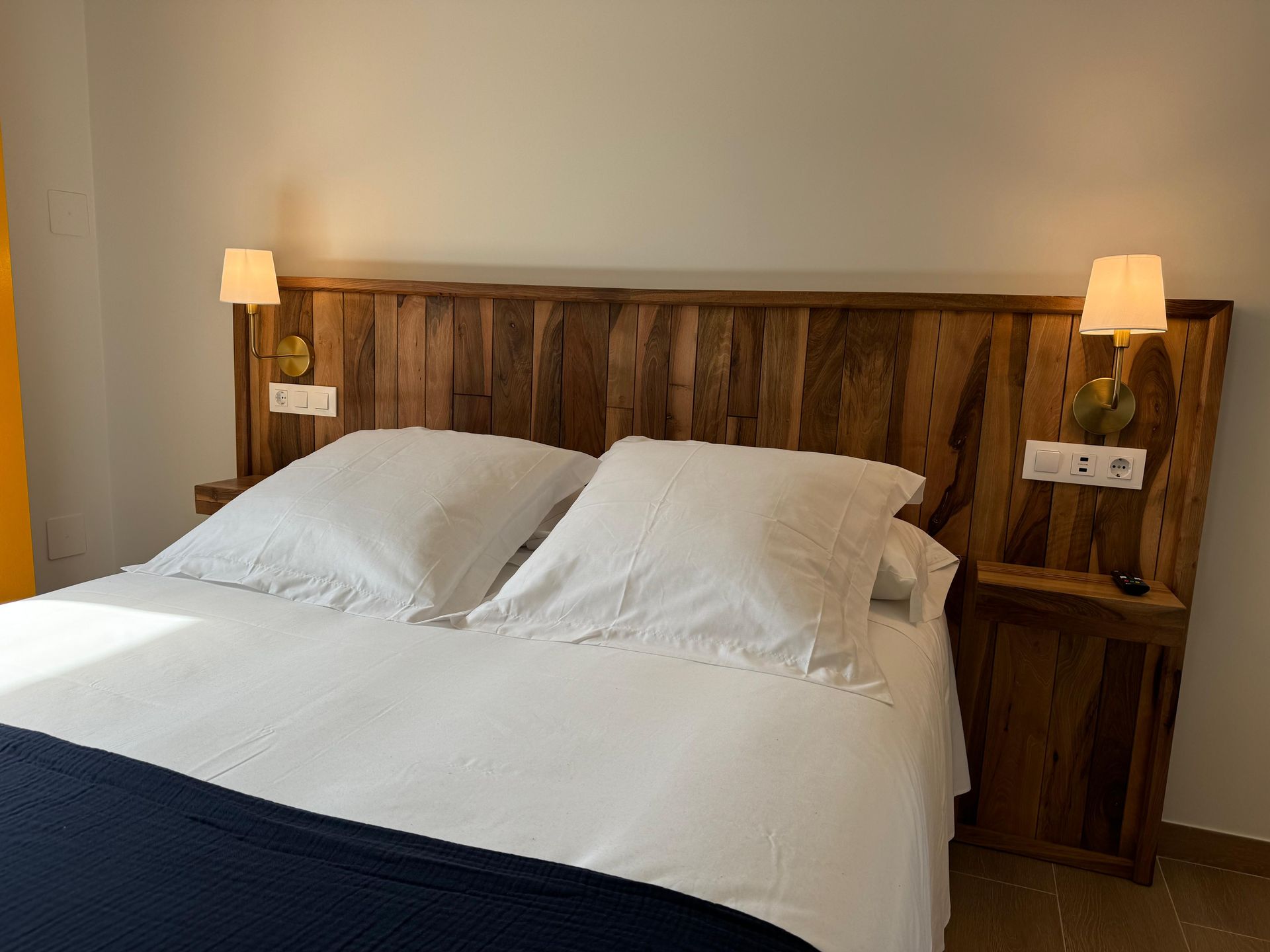 Dormitorio con cabecero de madera, ropa de cama blanca y dos mesitas de noche, cada una con lámpara.