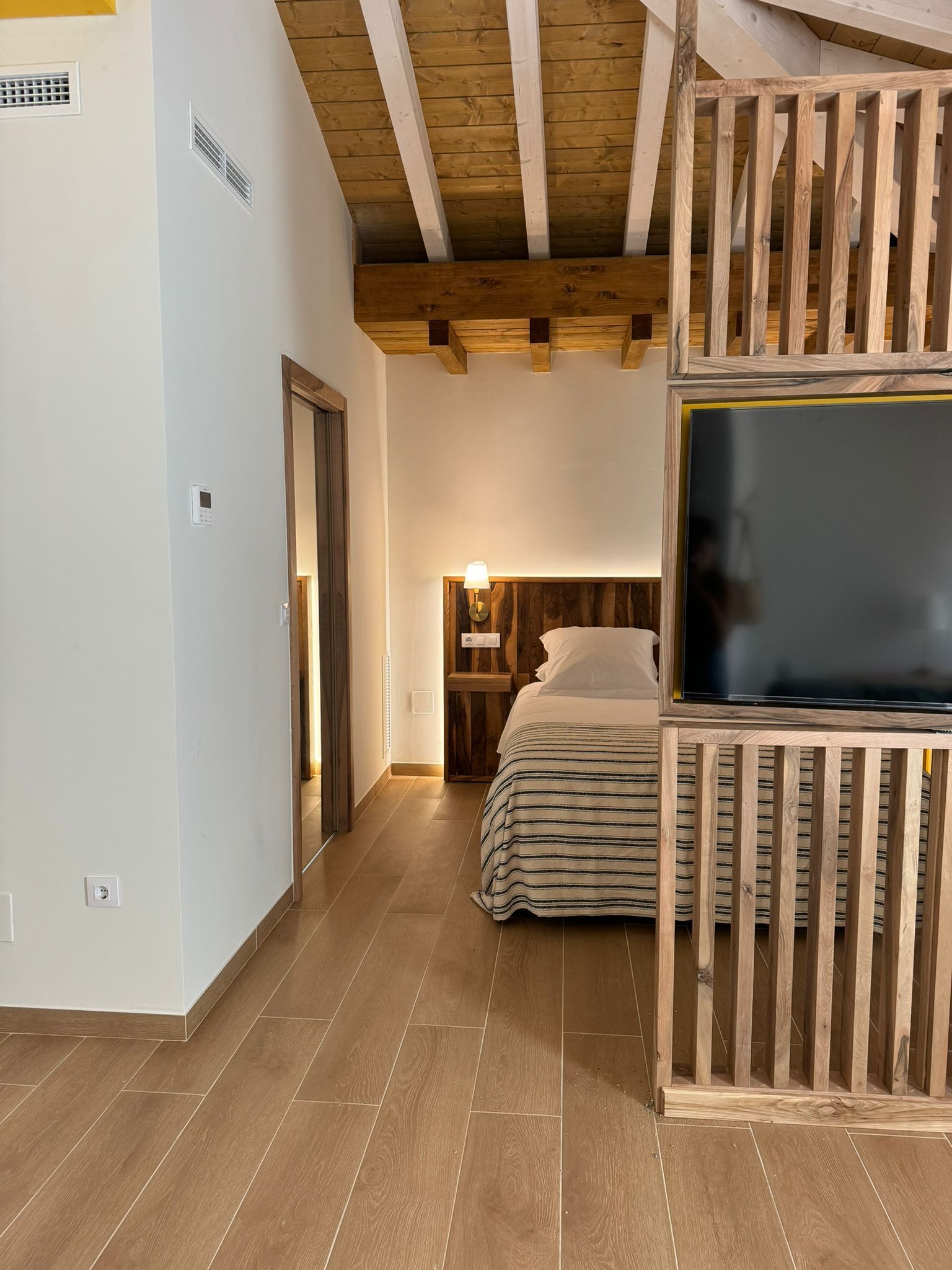 Dormitorio con vigas de madera, cama y pantalla de TV en estructura de madera.