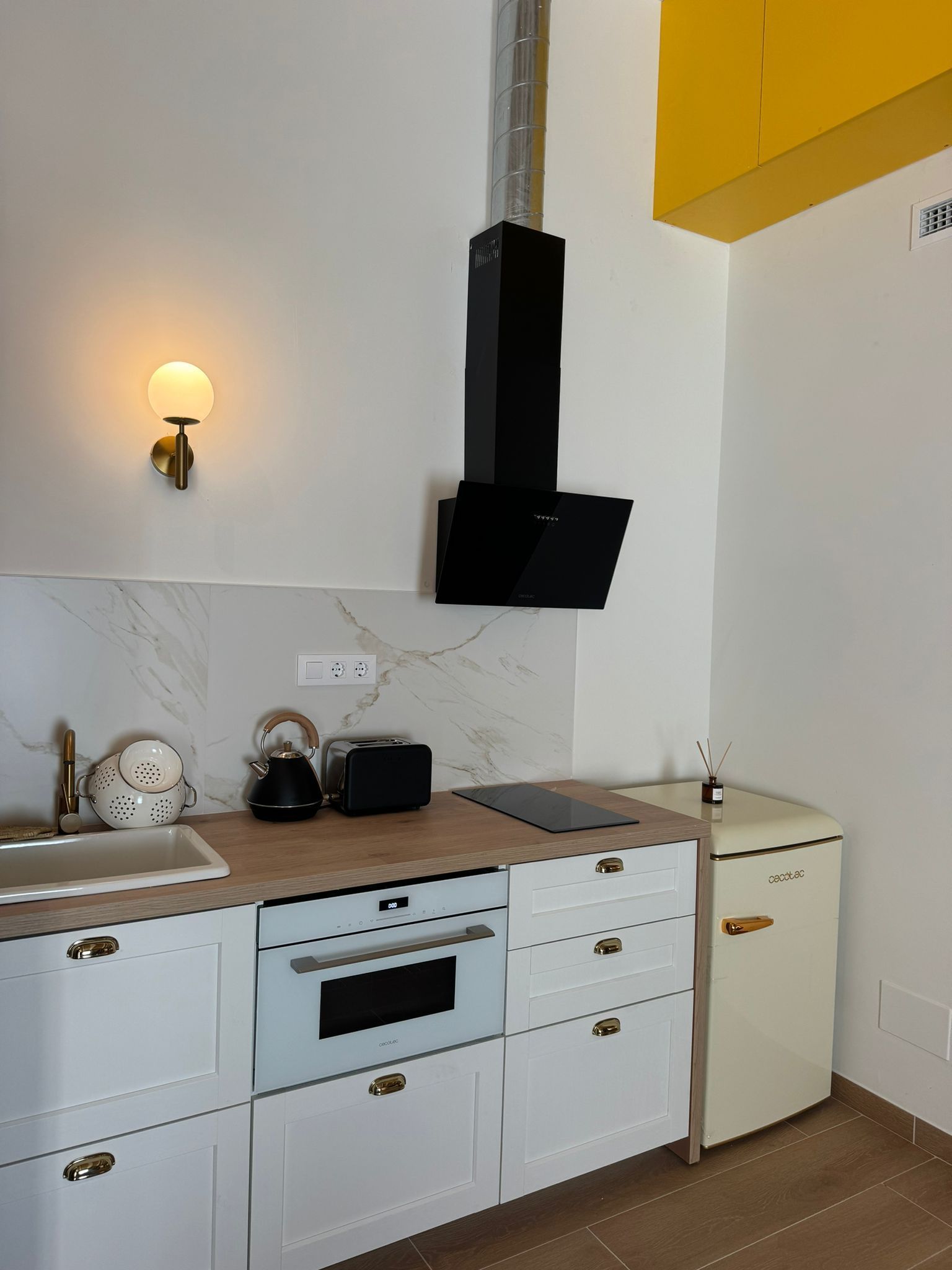 Cocina moderna con gabinetes blancos, campana extractora negra y detalles amarillos.