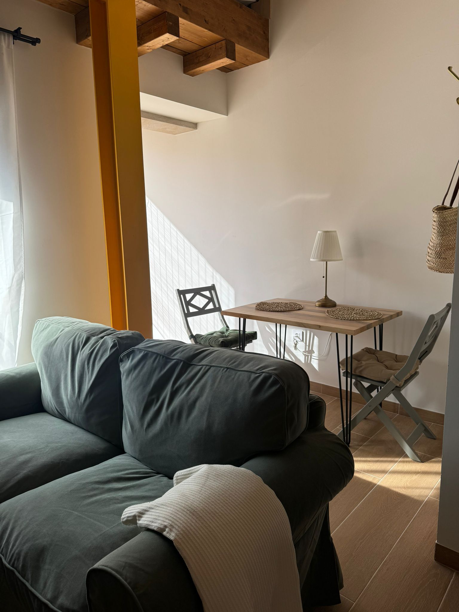 Acogedora sala de estar con un sofá verde, mesa y sillas. La luz del sol entra a raudales por la ventana,