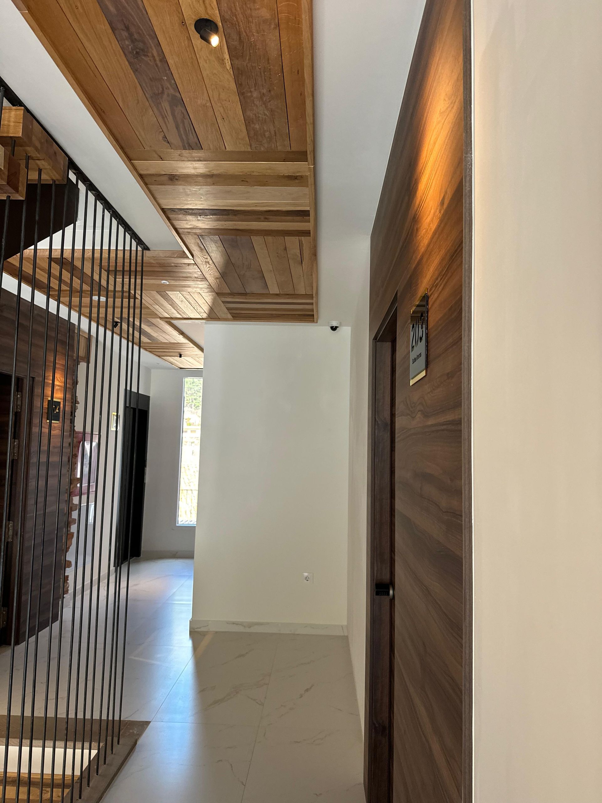 Pasillo con techo de madera, paredes blancas y puerta de madera.