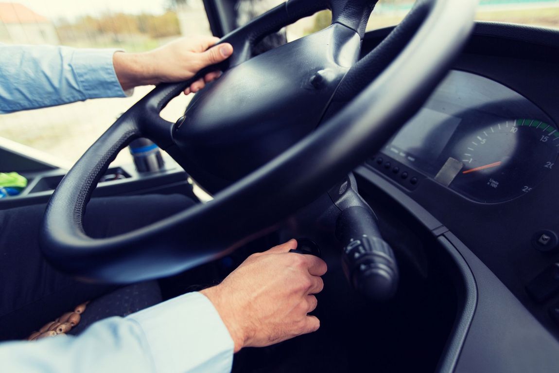 Primo piano delle mani di una persona che azionano il volante e la leva degli indicatori di direzione all'interno dell'abitacolo di un veicolo.