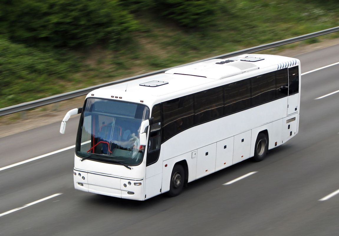 Un semplice autobus turistico bianco percorre un'autostrada a più corsie vicino a un terrapieno erboso.