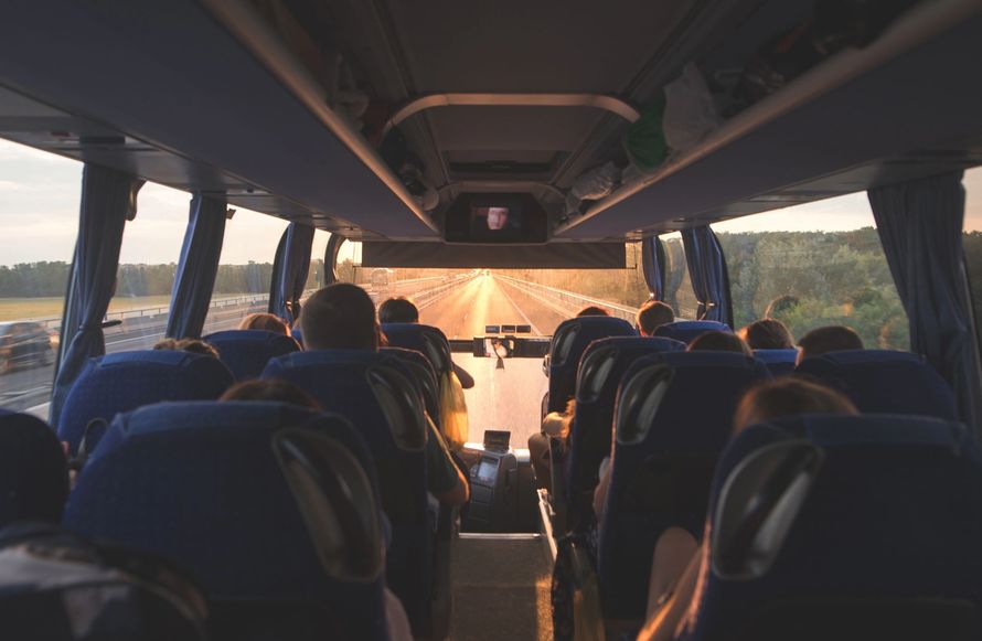 Vista interna dal retro di un autobus, con lo sguardo rivolto verso il finestrino anteriore di un'autostrada illuminata dal sole.