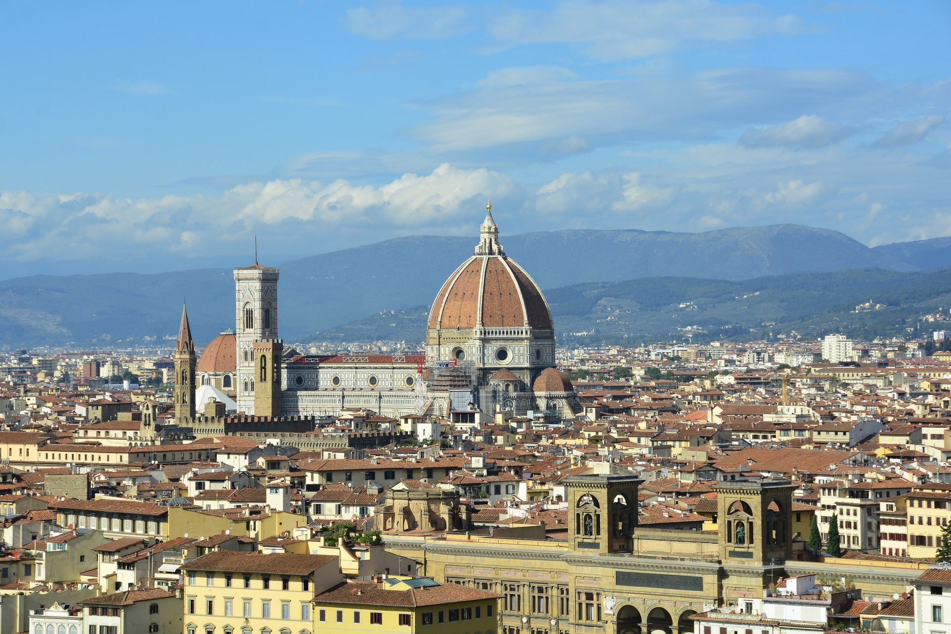 Veduta panoramica del Duomo di Firenze con la sua cupola in terracotta e il campanile che si ergono al di sopra di un fitto paesaggio urbano.