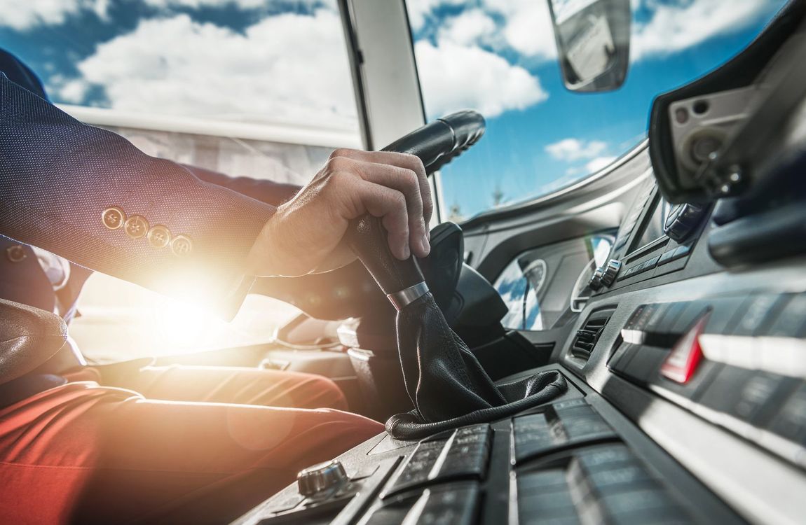 Le mani del conducente sul volante all'interno della cabina di un camion, con la luce del sole che filtra attraverso il parabrezza.