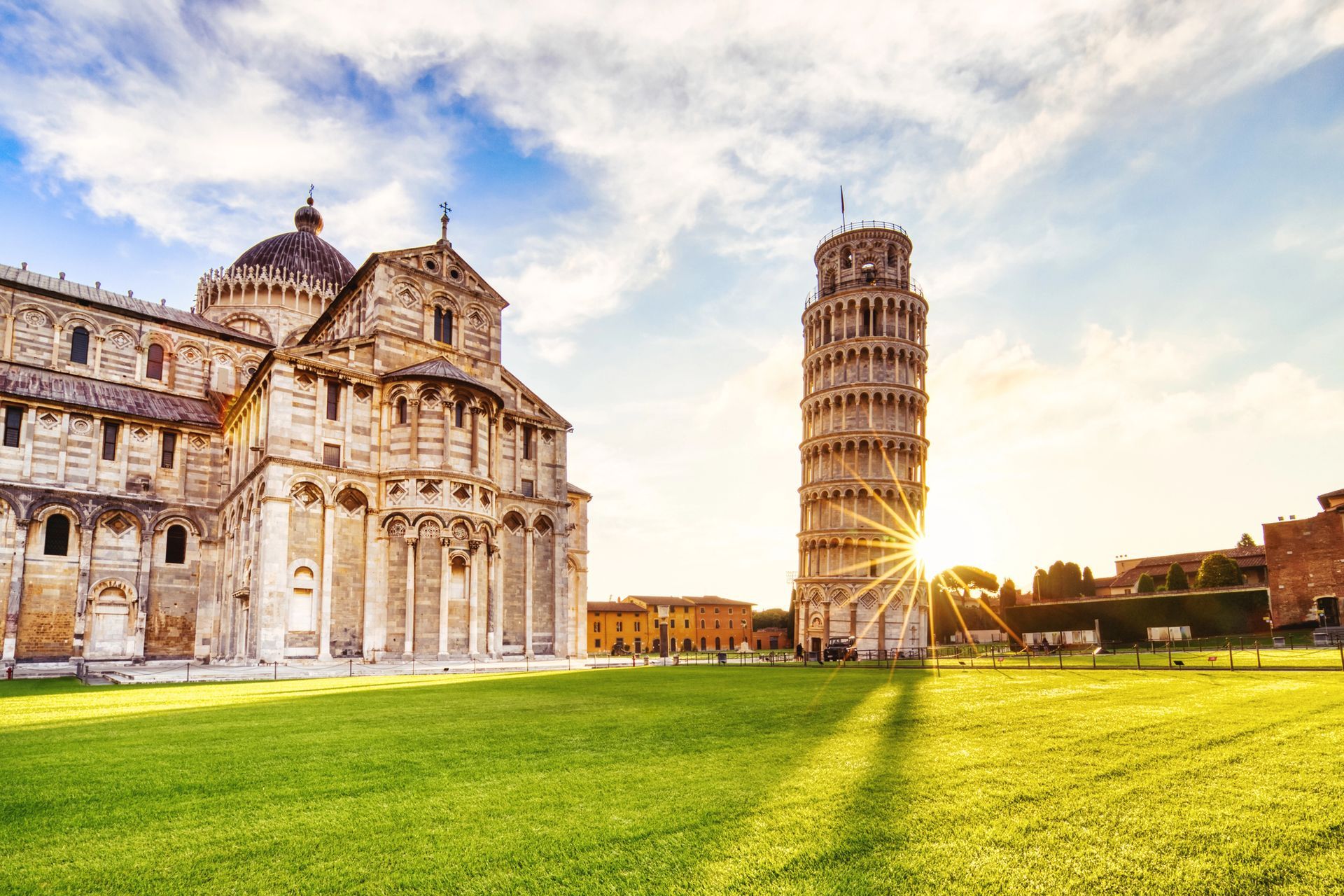 La Torre Pendente di Pisa si erge accanto al Duomo di Pisa, su un prato erboso sotto un cielo soleggiato.