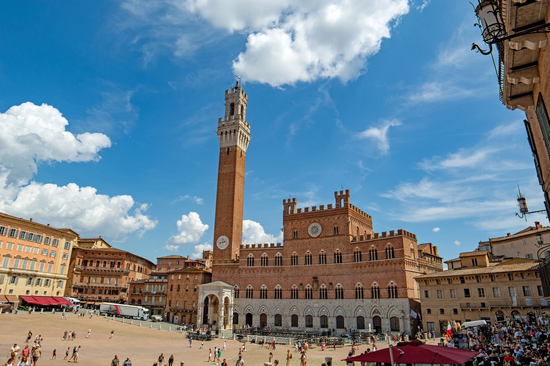 Una vista soleggiata e panoramica di Piazza del Campo a Siena, in Italia, con l'iconico Palazzo Pubblico in mattoni rossi e la sua torre.