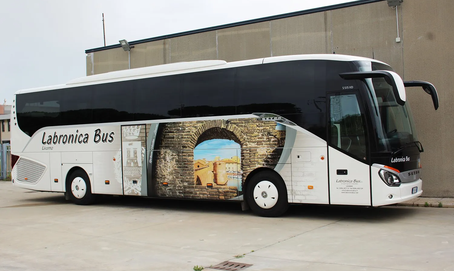 Vista laterale posteriore di un Pullman bianco con il disegno d’un monumento