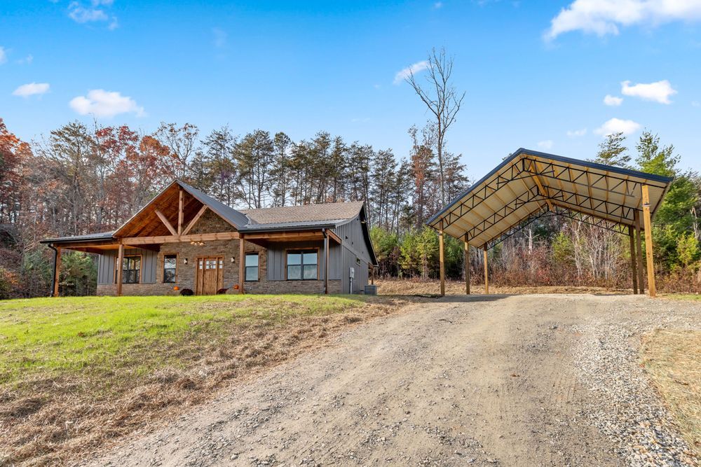 A house is sitting on top of a dirt road next to a carport.