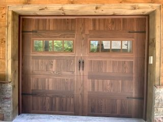A wooden garage door with two windows is sitting next to a stone wall.