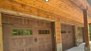A wooden garage with three garage doors and a porch.