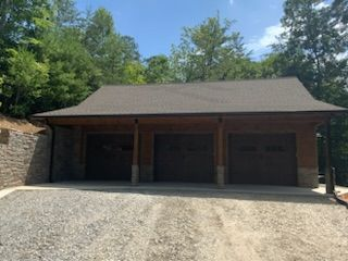 A large garage with three garage doors is surrounded by trees.