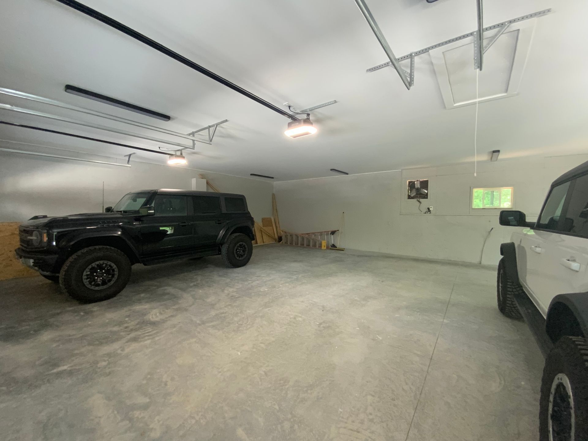 A black suv and a white truck are parked in a garage.