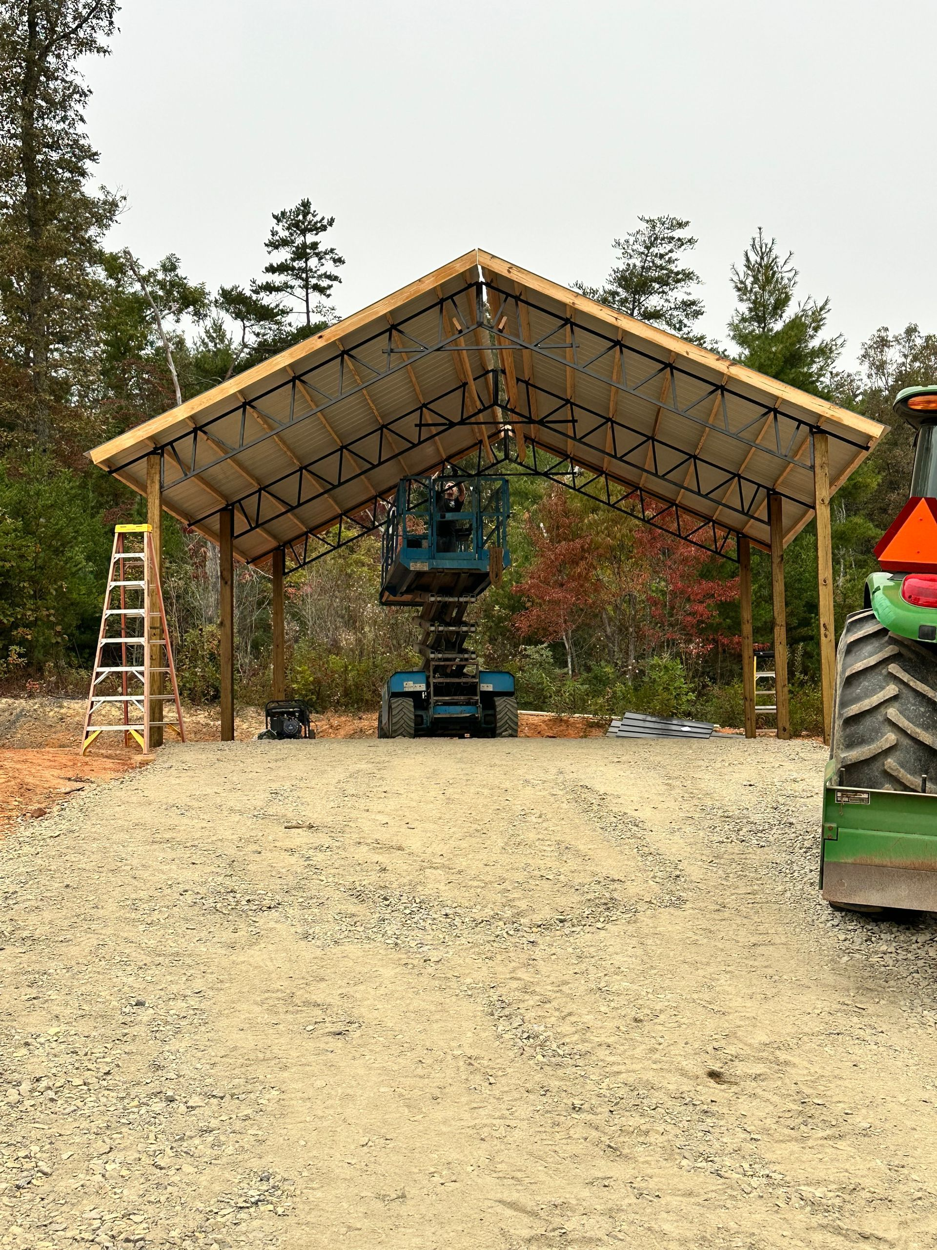 A green tractor is parked under a wooden structure.