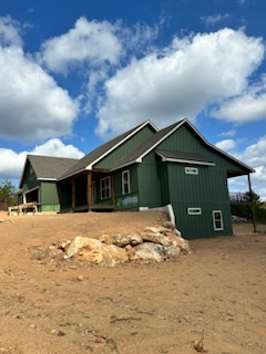 A green house sits in the middle of a dirt field