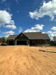 A green house with a gray roof sits in the middle of a dirt field