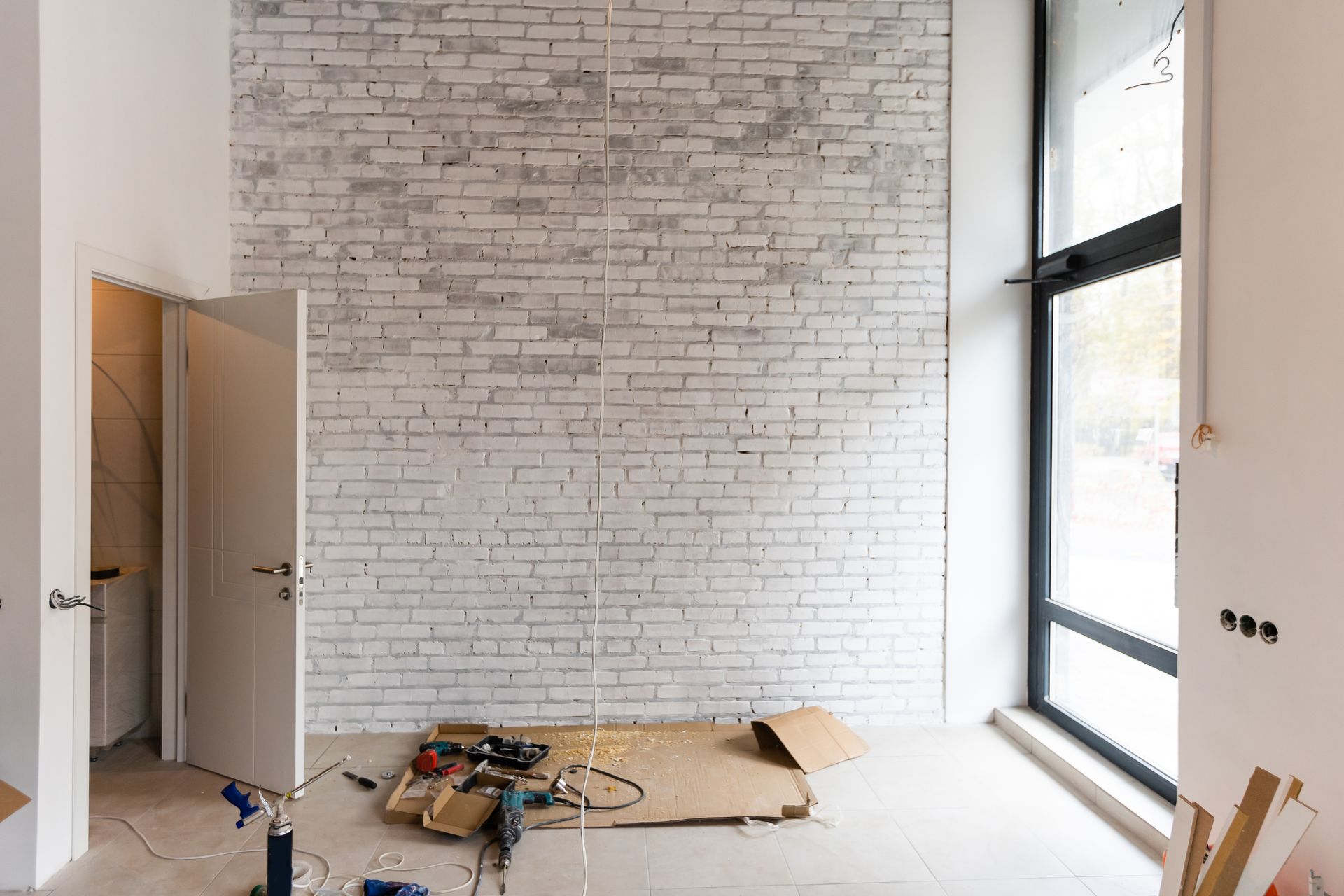 Partially finished room with white brick wall, open door, large window, and tools on the floor
