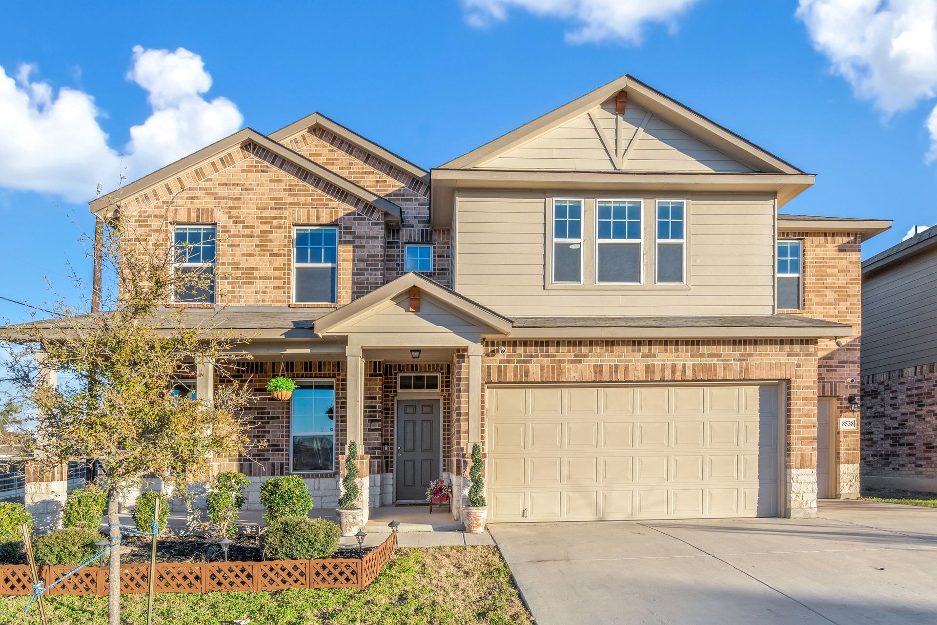 Modern two-story beige house with black trim, centered front door, and landscaped walkway