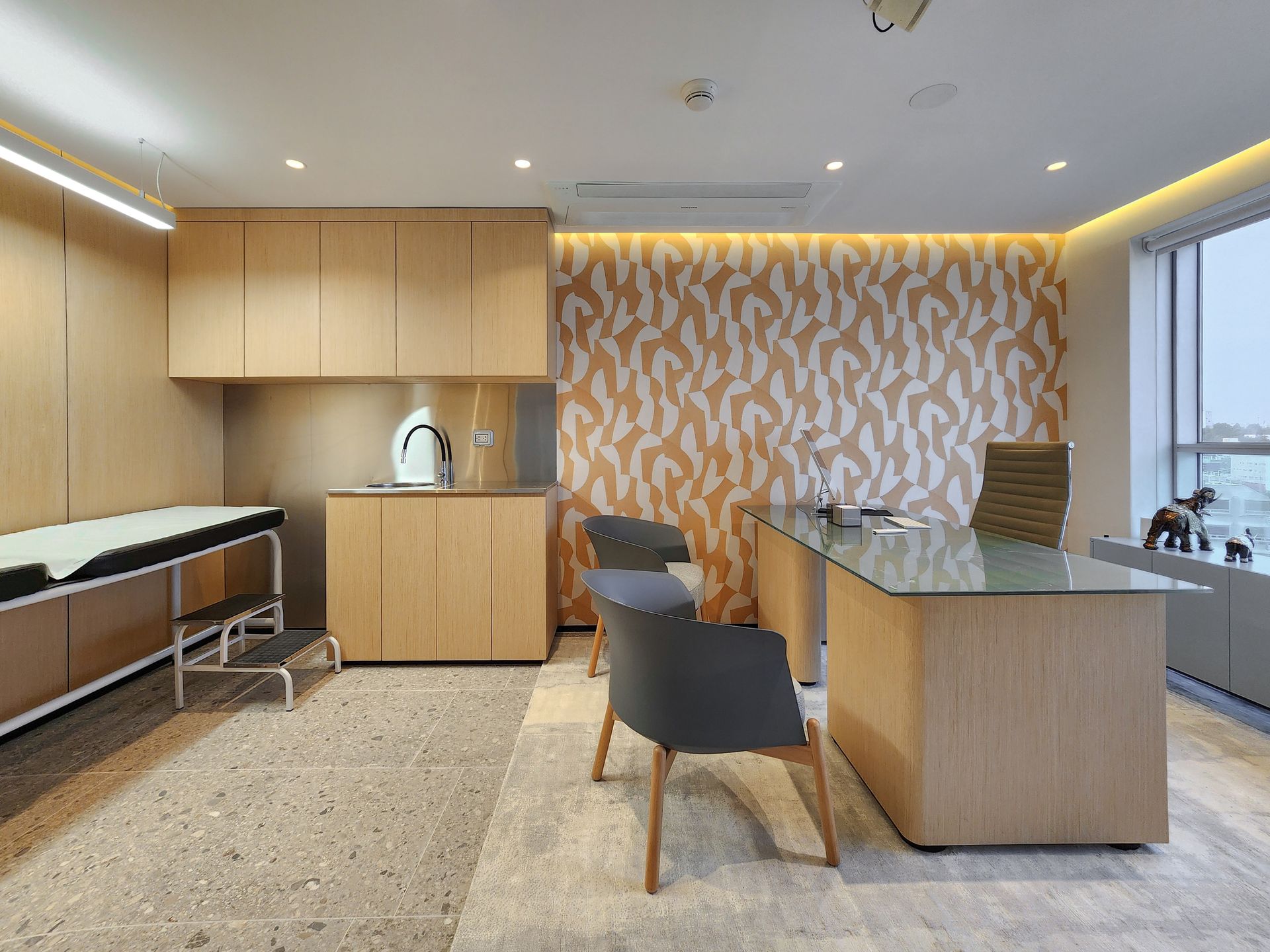 Un consultorio médico con un escritorio, sillas y una cama.