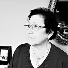 Una mujer que lleva gafas y un collar está sentada frente a un espejo.