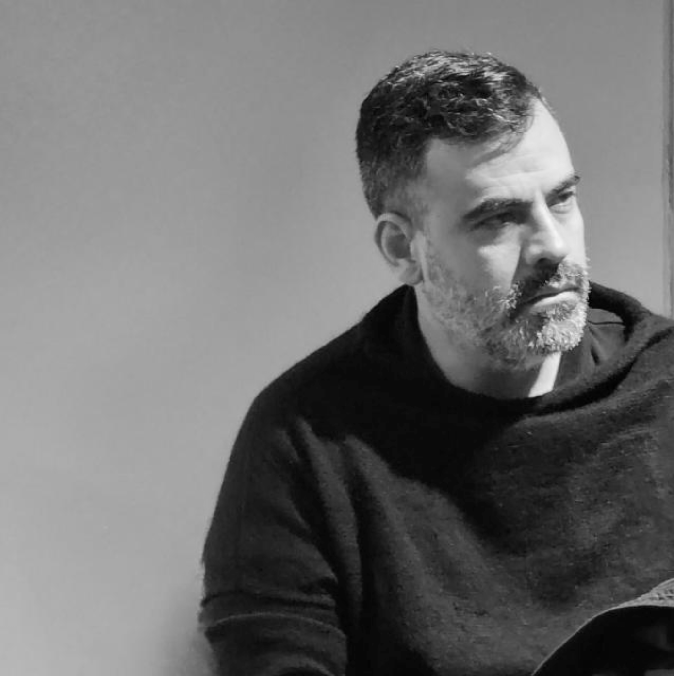 Un hombre con barba está sentado frente a una pared en una foto en blanco y negro.